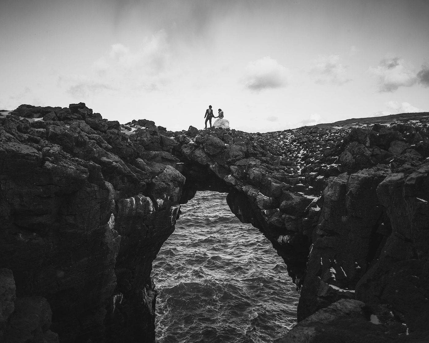 Couple standing on natural rock bridge over ocean