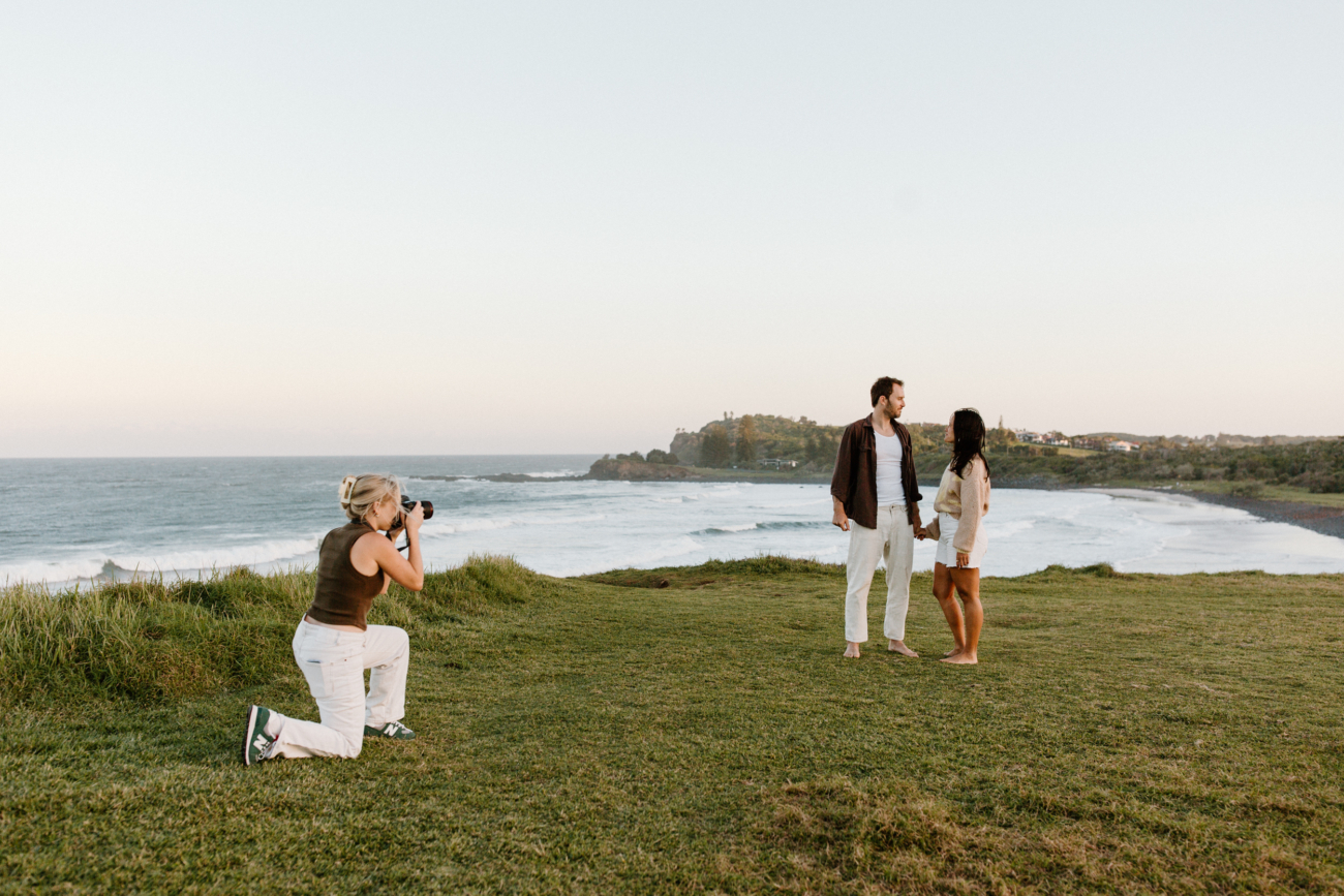 A photographer kneeling on a headland while a couple walk towards her